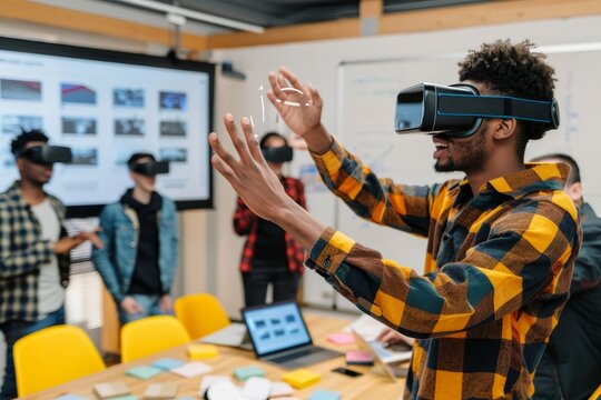 Young African man wearing virtual reality headsets and gesturing while standing at the desk with four multiethnic friends in a creative office.
