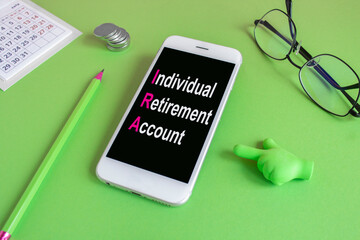 Concept words Individual retirement account on the mobile phone screen. Beautiful green background. Glasses, pen, coins. . Retirement savings, pension fund, passive income for grandparents. 