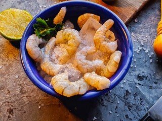 Clean shrimps in blue bowl with coarse salt , lemon and ice and gray background