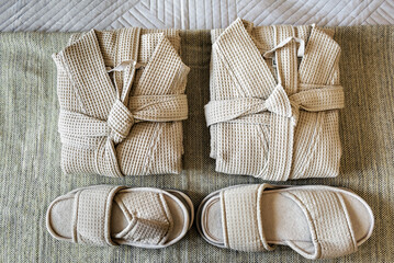 Close-up photo of neatly arranged bathrobes and slippers in beige rustic style. Soft, fluffy bathrobes are elegantly folded on textured wooden surface, complementing cozy, earthy tones of setting.  