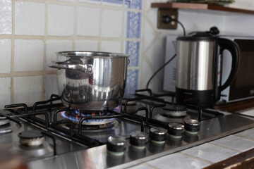 A pot boils on a gas stovetop next to an electric kettle