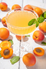 Apricot martini or margarita or lemonade cold fruit drink, summer iced fruit juice cocktail with mint and lemon, on white wooden table