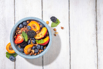 Granola breakfast with fruit and berry, summer whole grain tasty breakfast bowl with a lot of fruit and berries, with milk jug on white wooden table