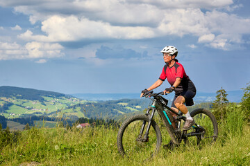 Obraz premium nice active senior woman riding her electric mountain bikeon Salmas summit in Oberstaufen, Allgaeu Alps , Bavaria, Germany 
