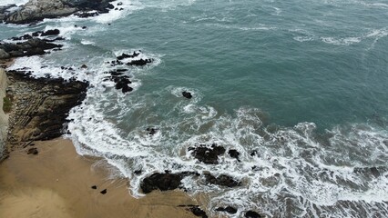 Drone photo of ocean waves reaching the sandy shore with rocks in Viña del Mar, Chile, capturing the serene coastal beauty from above