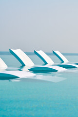 Pool chairs in a beautiful blue pool overseeing the sea
