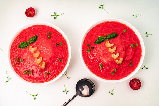 Cold Tomato Soup Gazpacho with basil, microgreens and celery in white cups on a light table. View from above.