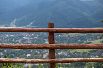 Obraz premium Green mountain slopes. Forest on the mountainside. A high wooden fence in front of a cliff.