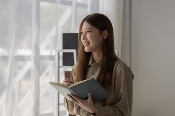 Fototapeta premium an Asian businesswoman is writing detail from the last meeting, there is a beautiful employee is smiling in the workplace, taking a note into the book witch is the first draft of report