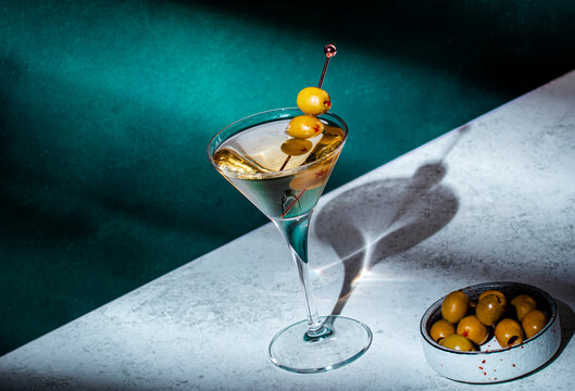 Martini, alcoholic cocktail drink with vodka, vermouth, olives on dark background, hard light