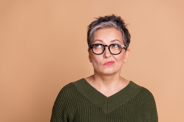 Photo of minded woman with short hairdo dressed khaki knit sweater in glasses look at offer empty space isolated on beige color background