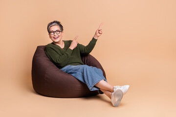 Photo of cheerful nice woman wear khaki stylish clothes sit soft bag recommend empty space isolated on beige color background