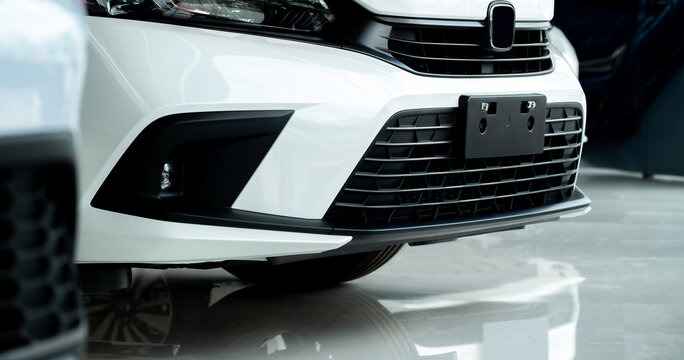 Close up front bumper and grille of modern white car in showroom, highlighting clean design, headlight detail, and stylish exterior for automotive industry, sales, and advertising use.