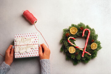 Christmas composition on a dark background: Beautiful female hands holding a gift liht box, A spool of red and white thread and two candy canes.