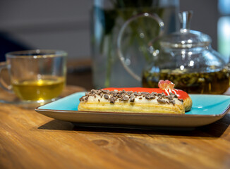 A plate of chocolate covered pastry sits on a wooden table next to a cup of tea
