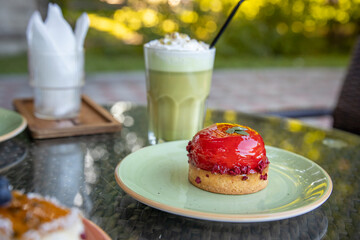 A freshly baked pastry with a red glaze on a green plate and green drink in a garden conveys a relaxing atmosphere