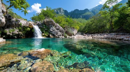 Fototapeta premium A tranquil turquoise lake with a small waterfall surrounded by lush greenery and towering mountains under a clear blue sky, inviting a sense of peace and natural beauty.