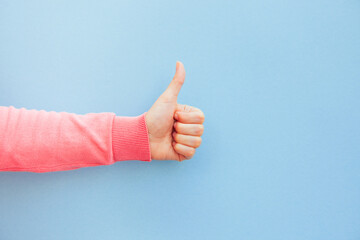 Woman hand in pink clothes is showing thumb up on blue background, motivation and success concept