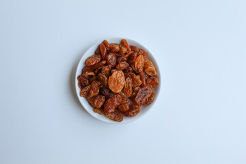 Raisins in small white plate, isolated on white background