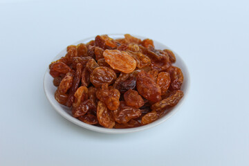 Raisins in small white plate, isolated on white background