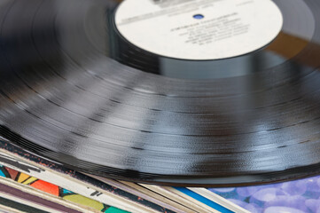 Close-up of a black vinyl record with grooves, resting on a stack of other vinyl records.