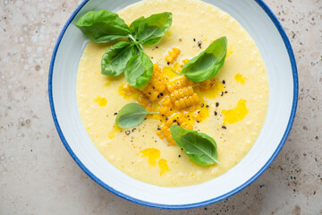 Blue and white plate with chilled gazpacho made of sweet corn, horizontal shot on a beige granite surface, high angle view