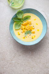 Turquoise bowl with chilled sweet corn gazpacho, top view on a beige stone background, vertical shot, copy space
