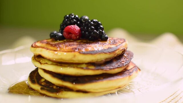 Desayuno de varios hot cakes con frutos rojos arriba y miel en un plato de vidrio 