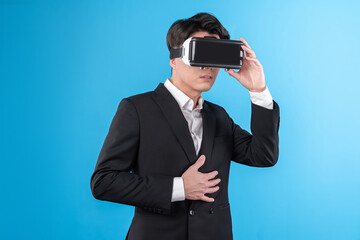 Smiling Asian businessman looking thorough VR connecting to business world report in futuristic metaverse, analyzing innovation technology ads in virtual reality isolated blue copyspace. Contrivance.