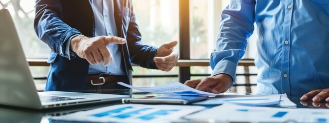 Two businessmen are reviewing documents and data at a desk in an office setting
