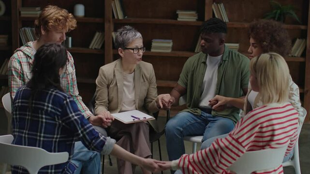 Therapy group participants engage in a supportive handholding activity, facilitated by a therapist, to build trust and connection