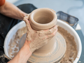 Close-up of a potter's hands making a ceramic vase on a potter's wheel. 