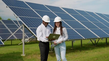 Two multiracial diverse female and male electrician engineers in safety helmet and uniform checking solar panels