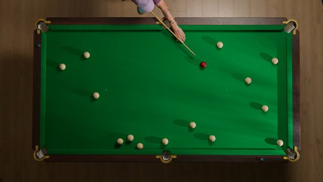 Top view shot of russian billiard green cloth table with red and white balls, person hitting the balls with cue.