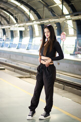 Young woman standing on a metro station platform and waiting for a metro train. People travel in public transport concept.