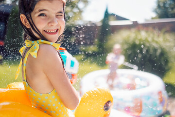 Joyful little girl in swimsuit with inflatable circle on terrace. Cute kids are messing around and...