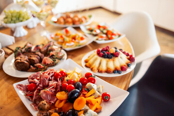 Close-up of delicious snacks on a wooden table in the dining room at home. Tasty hearty dishes. Sausage and cheese slicing with olives and tomatoes.