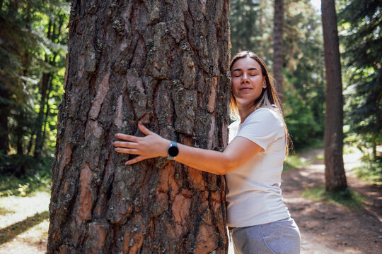A close-up portrait of a charming woman hugging a tree in the forest. An attractive girl gently touches the bark of a tree in the forest. - Powered by Adobe