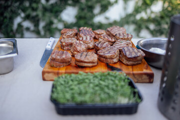 Close-up of delicious grilled beef burgers. Round tasty cutlets on a wooden board with green sauce. Cooking outdoors in the garden.