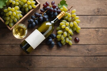 Obraz premium Unopened vintage bottle of white wine with blank label, empty wineglass & bunches of different grapes on wooden table background. Expensive bottle of chardonnay concept. Copy space, top view, flat lay