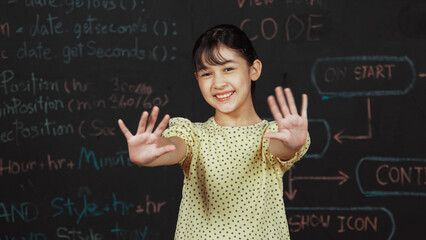 Cute happy girl waving to camera while standing at blackboard with engineering prompt or coding,...