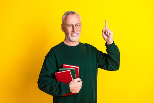 Photo portrait of nice senior man hold books point up eureka dressed stylish green clothes isolated on yellow color background