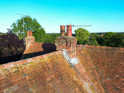 Drone image of an inspection of a very old brick built chimney on a listed property in rural Britain. The roof tiles show their age.