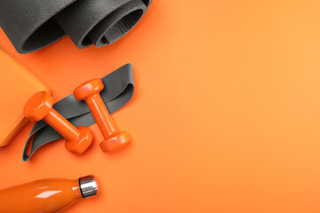 Dumbbells, yoga block, mat, thermo bottle and fitness elastic band on orange background, flat lay....