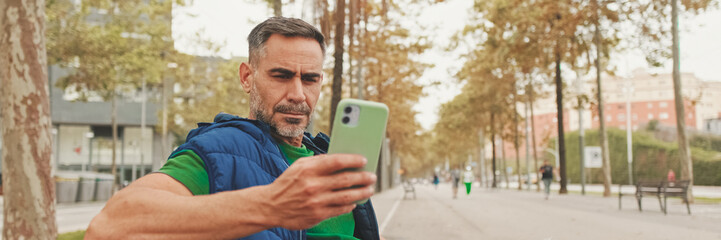 Mature man tourist wearing casual clothes sitting on bench scrolling smartphone