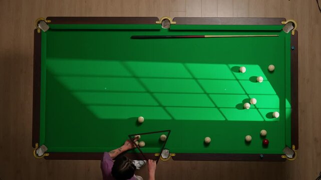 Top view full shot of russian billiard green cloth table with white ball being arranged in pyramid., person setting up the balls in triangle.