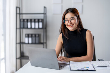 A woman is sitting at a desk with a laptop and a clipboard