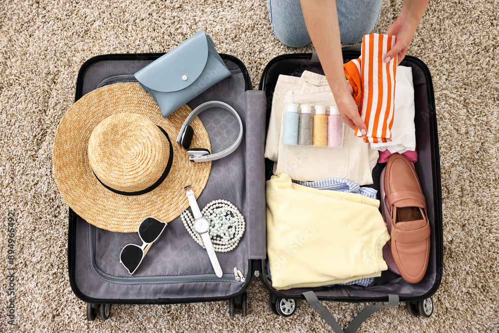 Wall mural Woman packing suitcase for trip on floor indoors, top view