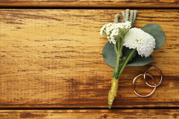 Small stylish boutonniere and rings on wooden table, flat lay. Space for text