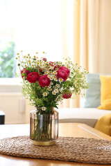 Beautiful ranunculus flowers and chamomiles in vase on table indoors